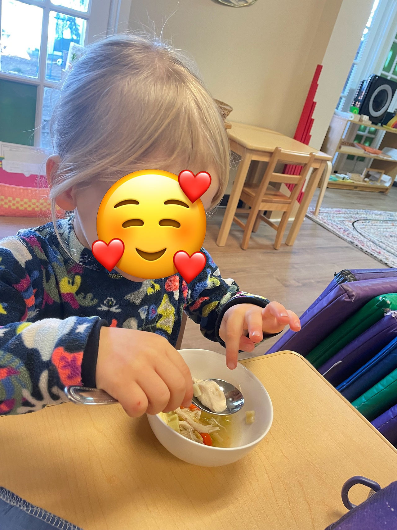 A 3 year old girl using her finger to put a chicken on a spoon from the soup bowl