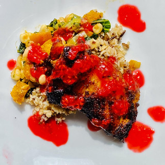 Nicely plated on a white plate with Pan Seared Chicken Thigh with Roasted Root Vegetables, Wild rice and raspberry sauce on top