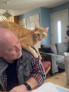 Orange tabby cat on Aric's shoulder and back.