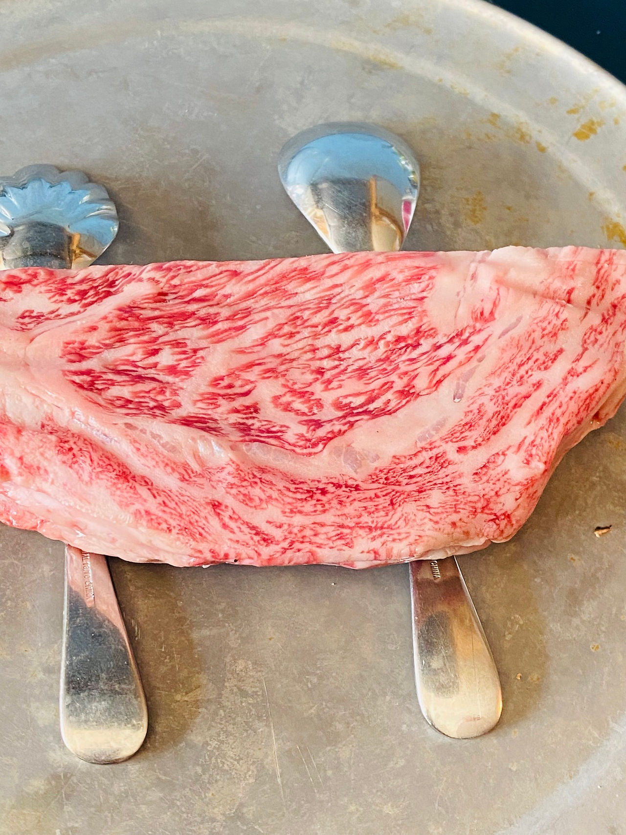 Wagyu by Brunson Meat Co sitting on top of two upside down spoons on a silver plate, raw.