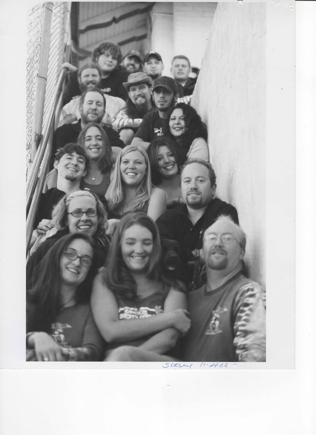 Black and white photo with many people sitting on the stairs smiling for the camera