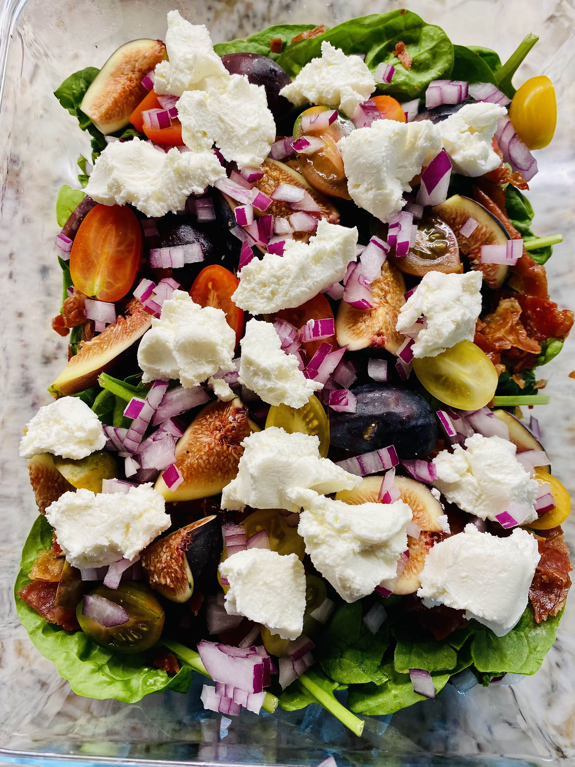 Spinach and Fig Salad with Grape Tomatoes cut in half, finely minced Red Onions, Crispy Prosciutto, Goat Cheese in a rectangular container