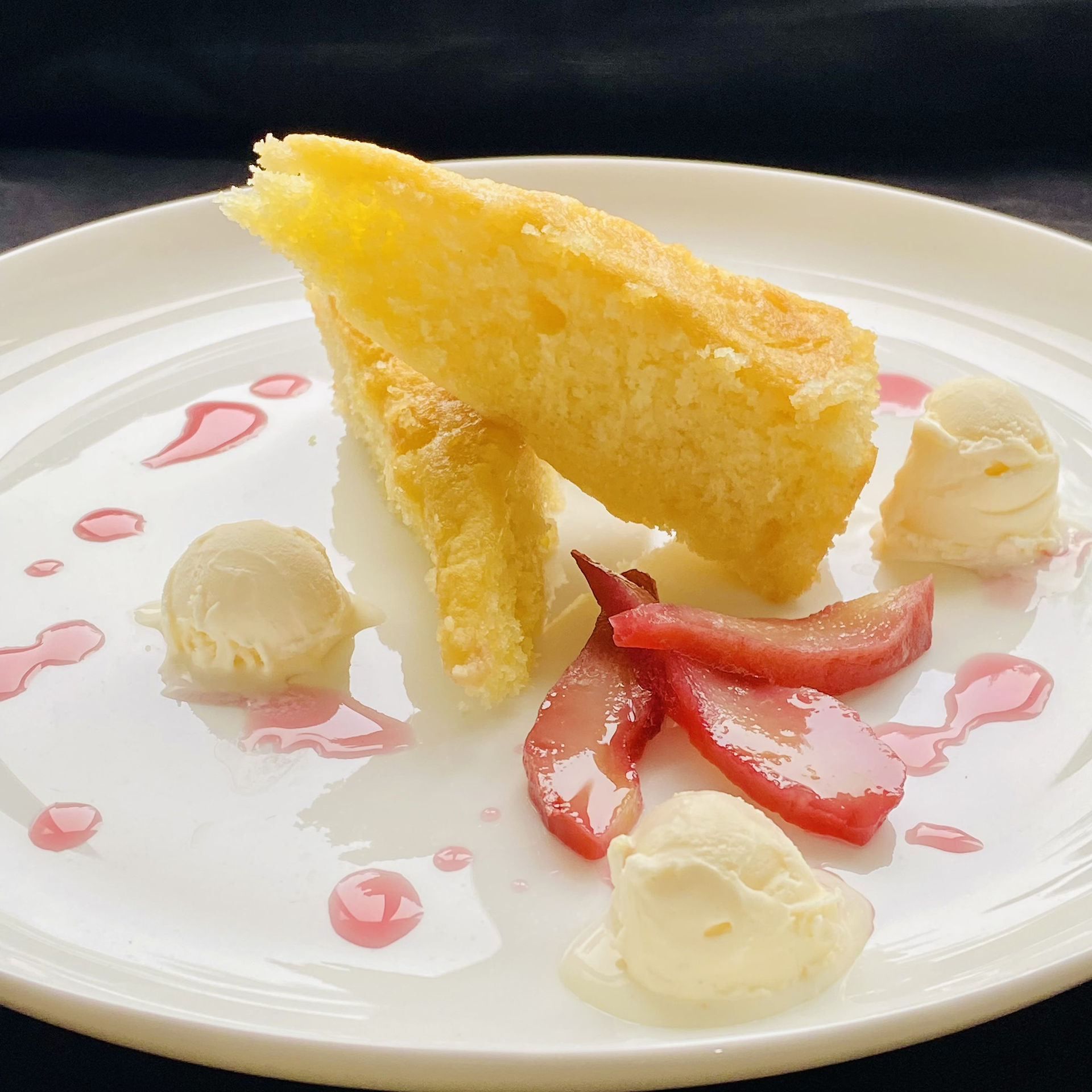 Olive Oil Cake. Two Pieces of Olive Oil Cake, cut in triangulary on a white dish, Port Poached Pear and Vanilla Ice Cream, Sweet Port Sauce around the dish.