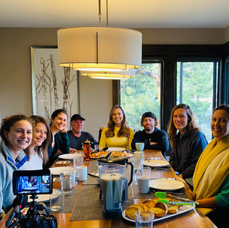 6 women and 2 men sitting over a dinning table, smiling for the photo