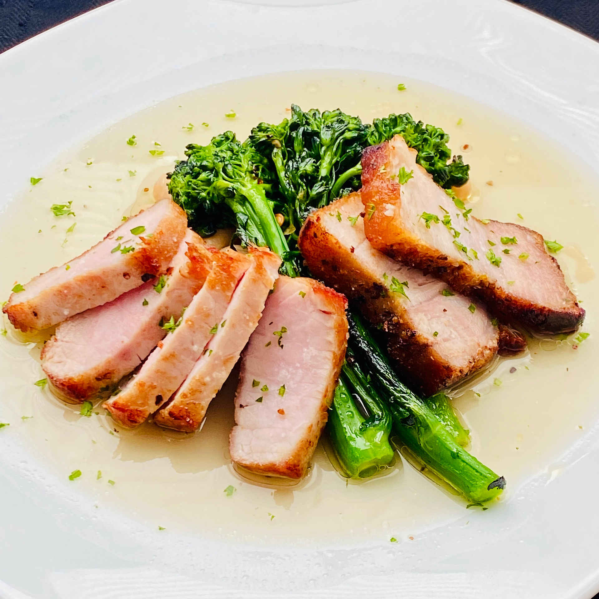 Pork Two Ways with Broccolini on white plate sitting on a white sauce.