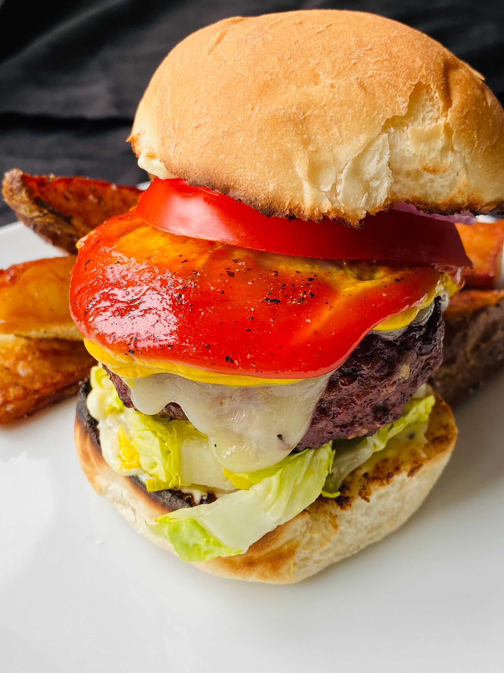 Classic Burgers& Potato Widges. Burger has giant tomatoes, lettuce, cheese, and a bun.