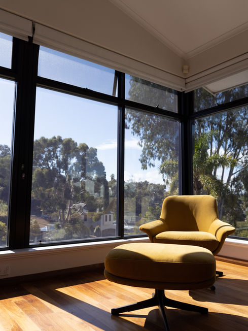 Mustard velvet chair in open plan living room with floor to ceiling windows offering beautiful suburban views