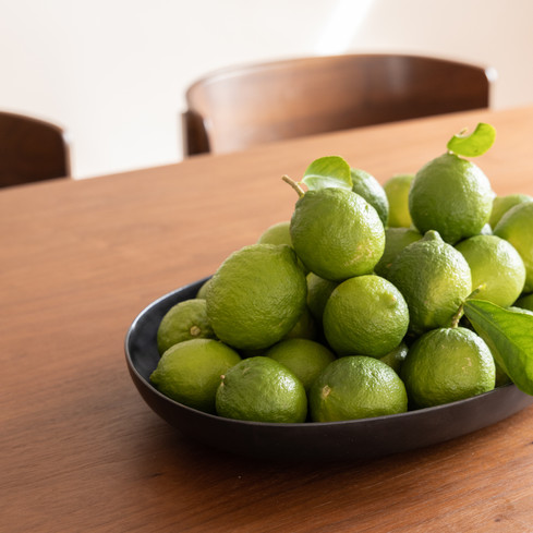 Styled wooden dining table with a black bowl of fresh limes