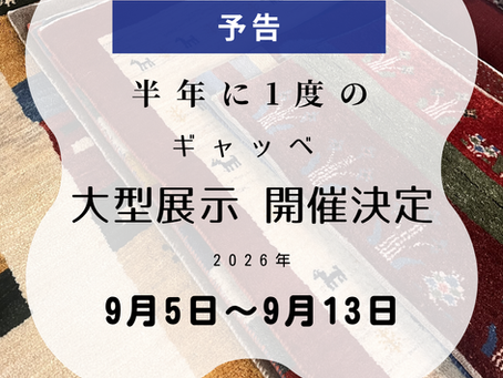 赤やベージュ、紺色など、色とりどりのあたたかみのある手織りギャベ絨毯が何枚か重なって敷かれている写真。上下には薄いピンクとブルーのグラデーションの帯があしらわれています。中央の白い半透明のやわらかな枠の中に、2026年9月5日から9月13日まで、半年に一度のギャベ大型展示の開催が決定したことを知らせる予告の文字が大きく書かれています。画面の下部には、ありかわ家具のロゴと、山形市十日町の店舗情報、お電話番号が記載されています。