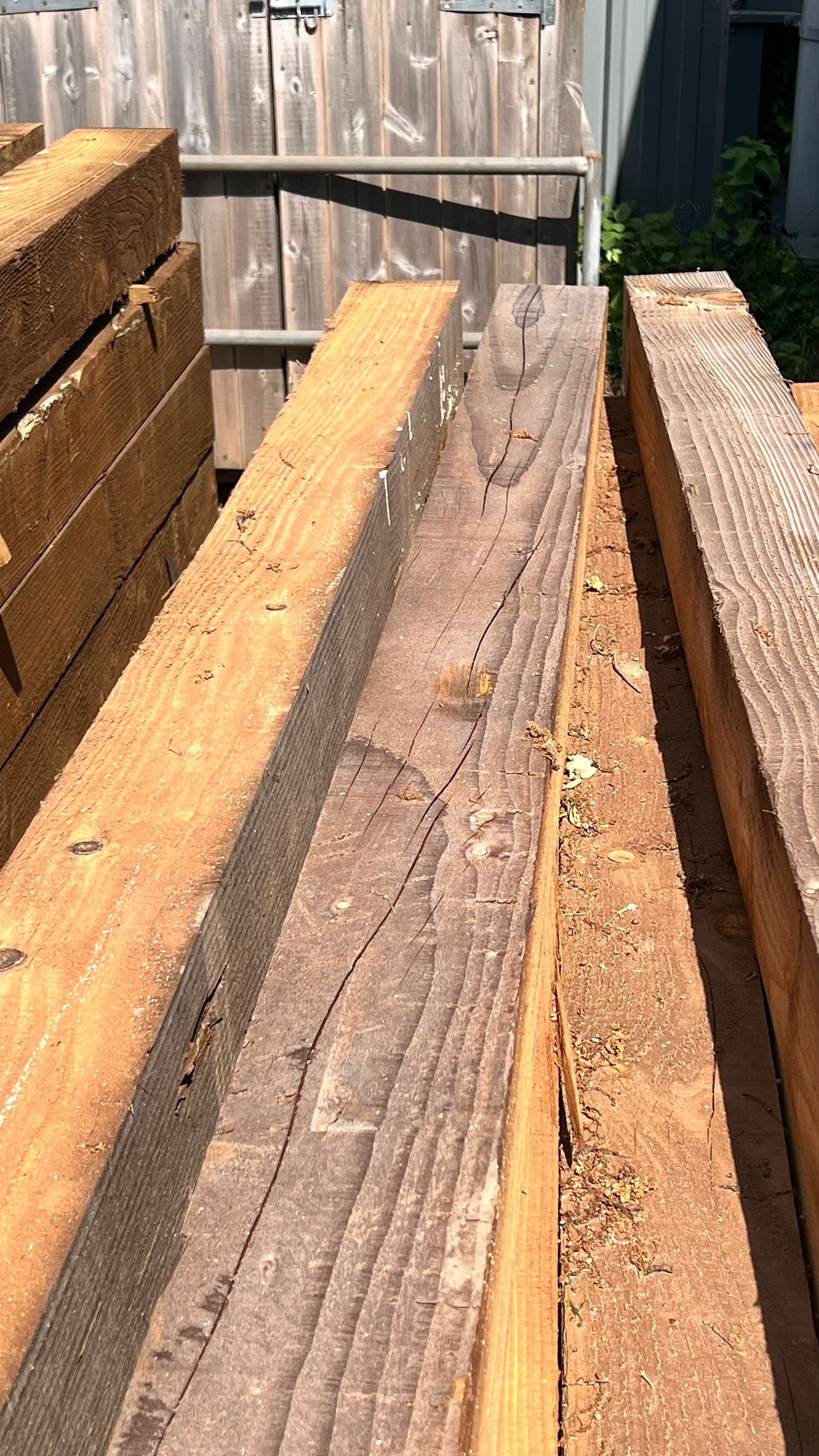 A top-down view of several large, rectangular wooden beams or railroad ties, showing varying shades of brown and natural wood grain.