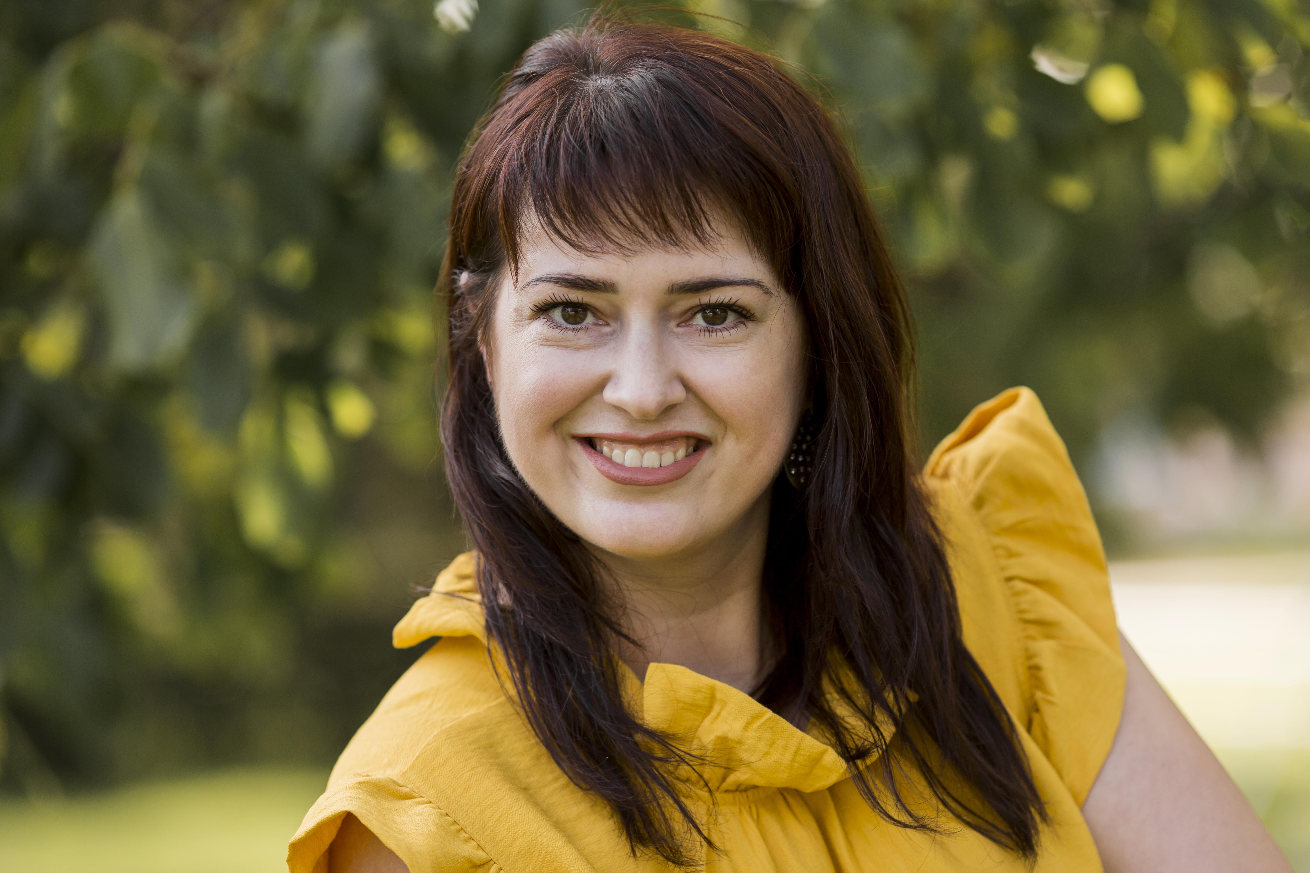 Smiling woman with long brown hair in a yellow blouse