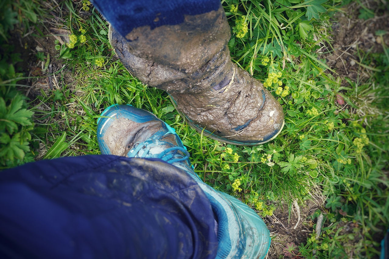 Zwei stark verschmutzte Wanderschuhe auf feuchtem Wiesengrund – Zeugnis einer matschigen Wanderung im Calfeisental