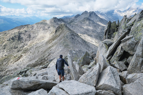 Wanderer beim Abstieg vom Sidelhorn über Blockgelände entlang des Grats, rote Wegmarkierung sichtbar, im Hintergrund die Berner Alpen