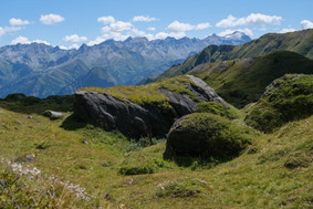Weiche Alpwiesen mit moosbewachsenen Felsblöcken und weitem Bergpanorama beim Lago Retico