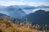 Weites Panorama mit Morgennebel beim Aufstieg zum Lago Retico, trockene Gräser im Vordergrund