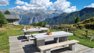 Granitsteintische auf der Terrasse der Bovarinahütte mit weitem Bergpanorama Richtung Surselva