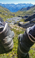 Wanderpause mit Blick auf zwei Wanderschuhe, weites Bergpanorama Richtung Surselva dahinter