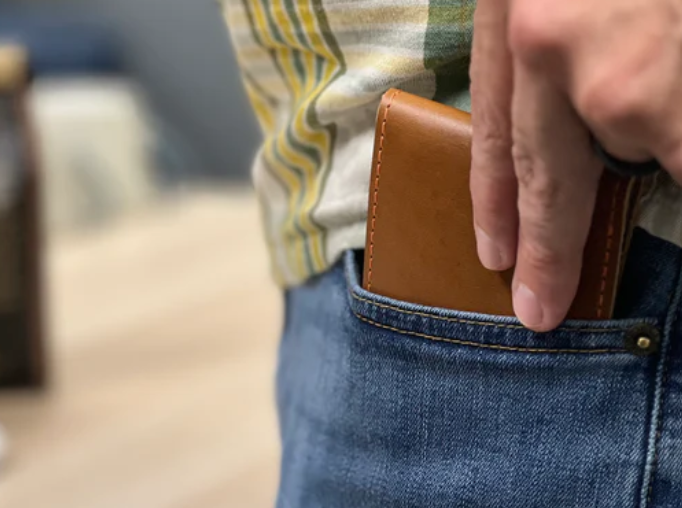 Man putting his men's leather bifold wallet into his jeans back pocket