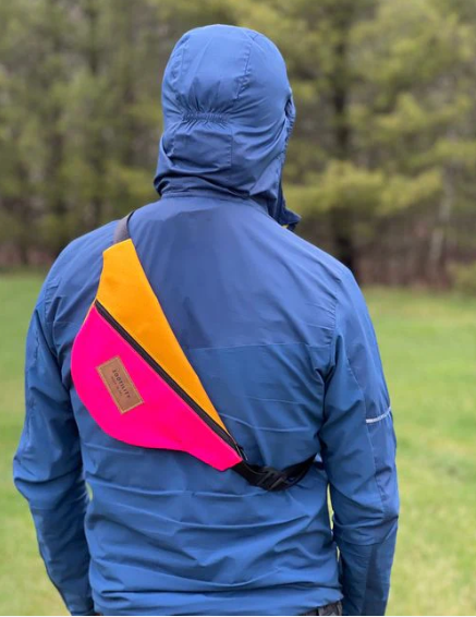 Man hiking with sidewinder sling in hot pink/mango over his back on top of his raincoat