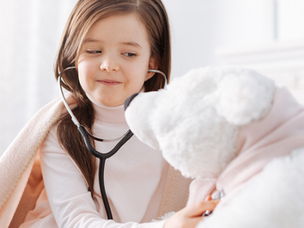 A little girl pretending to be a doctor, examining a stuffed toy with care and empathy during role-play.