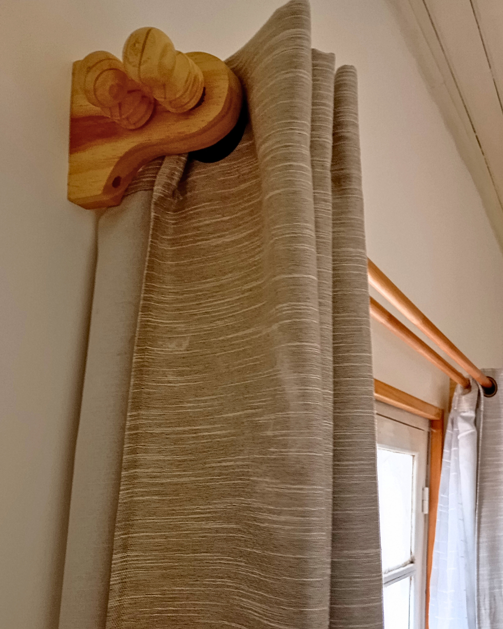 Cortina blanca colgada de una barra de madera clara en un ambiente iluminado. Ambiente sereno y minimalista.