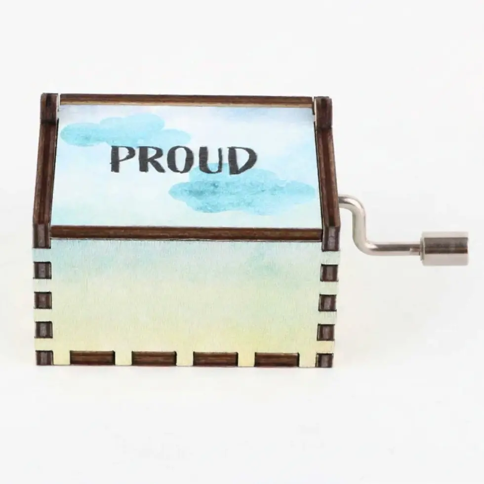 Thumbnail: Rainbow wooden music box with 'PROUD' painted on the lid amidst soft blue clouds.
