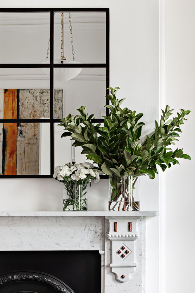 Classically detailed marble fireplace with black framed mirror above. Two vases of flowers sit on top of the mantel piece.