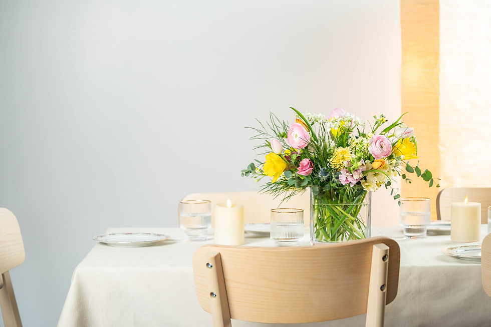 Mountain Laurels signature flower bouquet in vase on a dining table with candles. Wooden chairs, soft light, and minimal decor create a cozy ambiance.