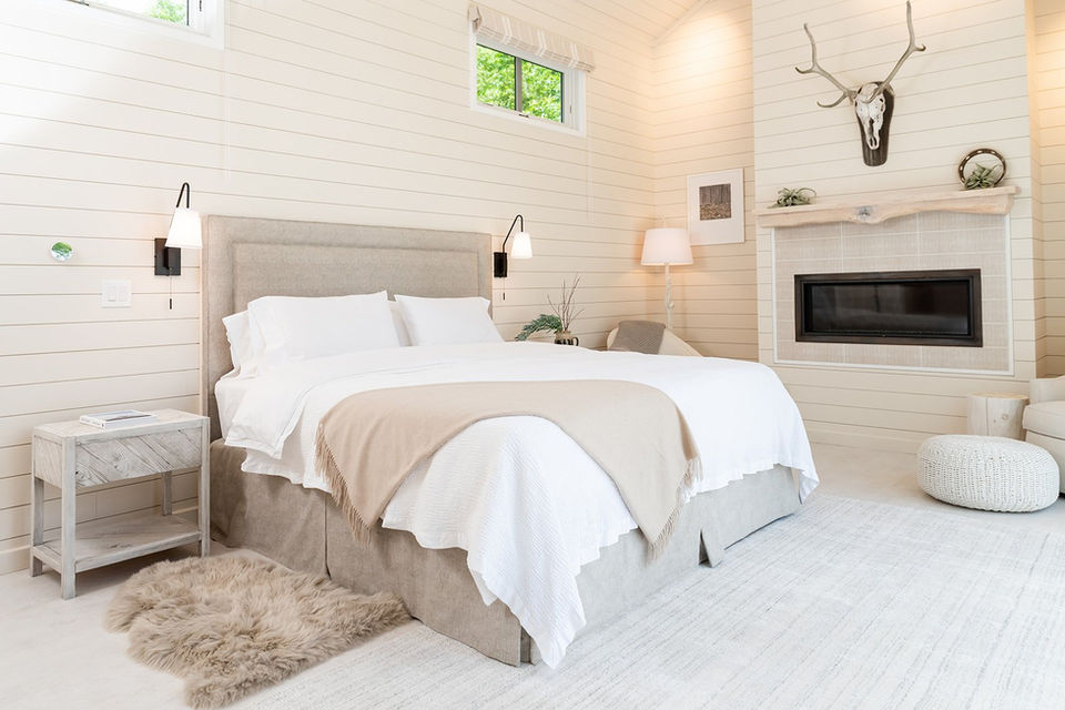 A serene, custom-designed bedroom with shiplap walls, neutral tones, and a fireplace, reflecting the warmth of a historic home restoration.