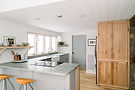 A bright and modern kitchen featuring light wood cabinetry, white shiplap ceilings, and a sleek gray island with a built-in cooktop. Open shelving and large windows allow natural light to fill the space. Sawteeth Carpentry specializes in custom remodels and historic restorations in upstate New York, Essex, and the Lake Champlain region.