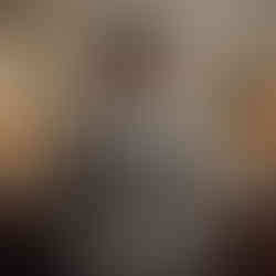 Handsome man in light grey suit stands elegantly between two lamps.