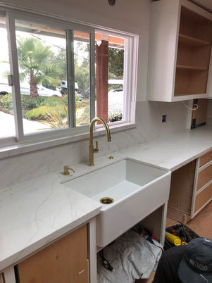 Close-up of a luxury white apron-front farmhouse sink paired with a brushed brass gooseneck faucet.