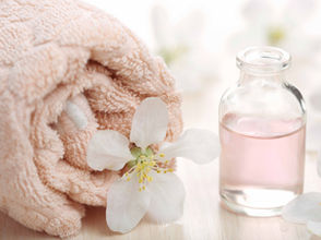 Agua Floral en botella de cristal, flores blancas alrededor y una toalla rosa.