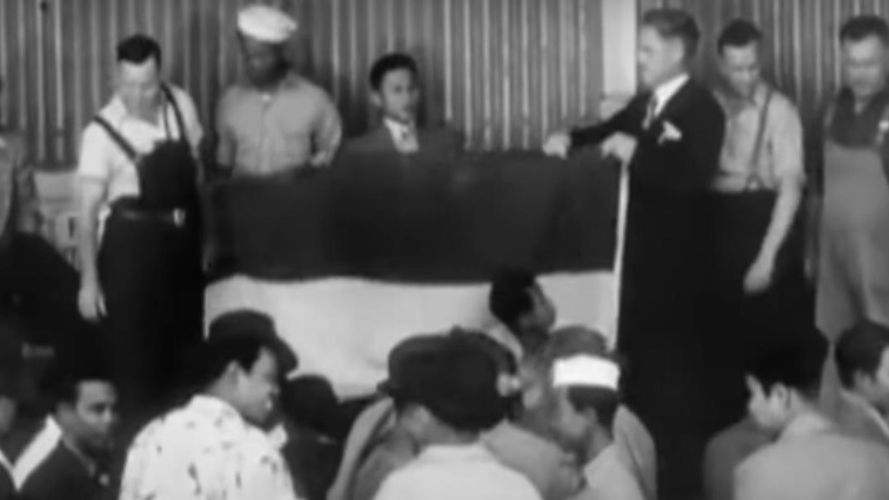 Sekretaris federal Perserikatan Buruh Pelaut Australia memberikan bendera merah putih kepada wakil buruh Indonesia sebagai bentuk dukungan kemerdekaan Indonesia. (Film Indonesia Calling karya Joris Ivens).