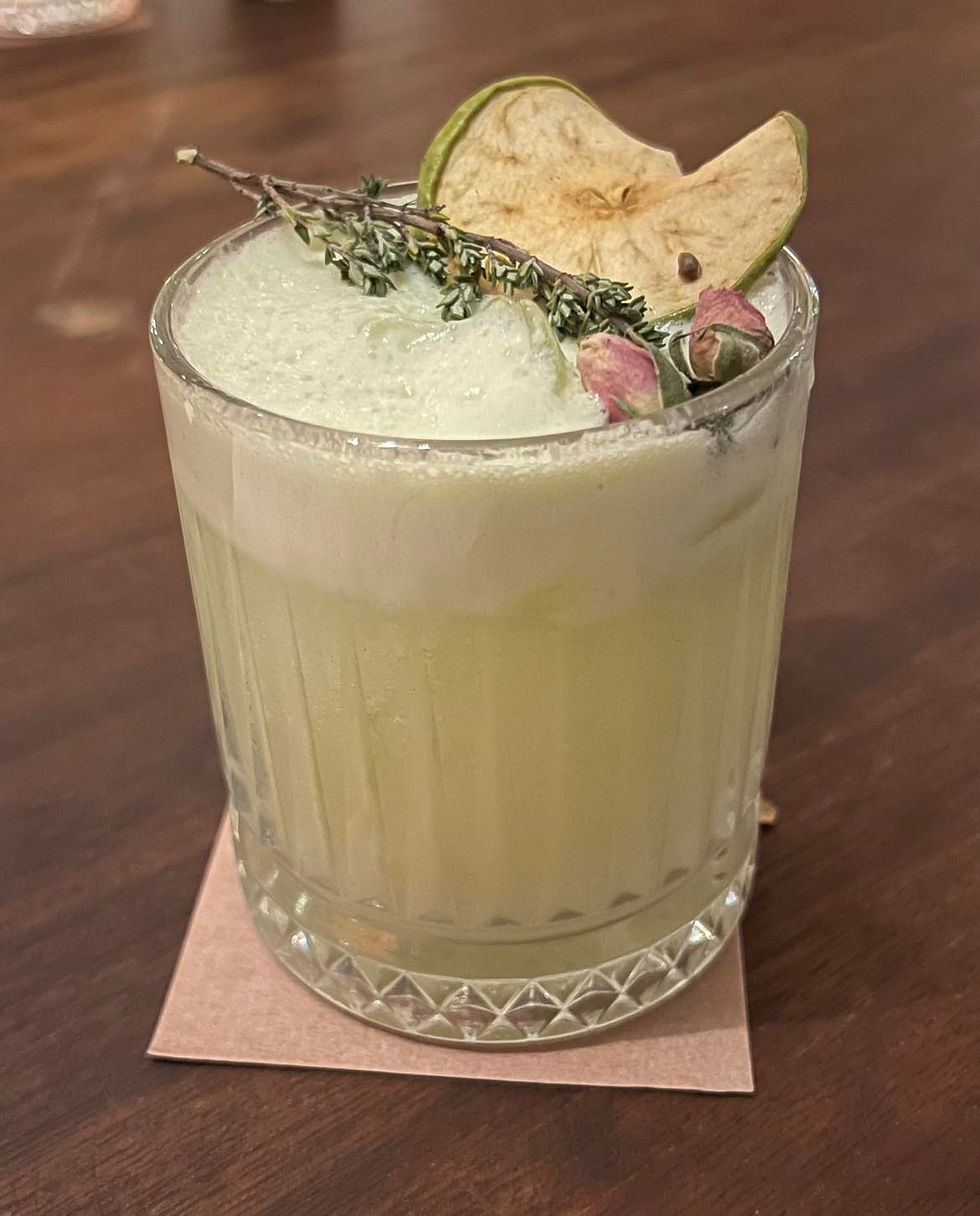 A cocktail garnished with dehydrated apple and thyme