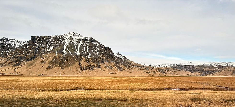 Snow-capped mountains under a cloudy sky, with vast golden fields in the foreground. The scene feels tranquil and expansive.