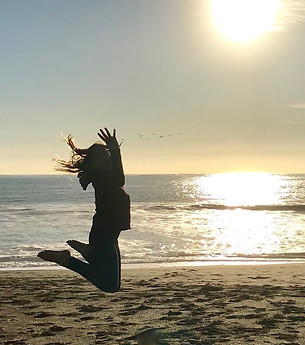 Woman jumping on the beach at sunset - joy and freedom