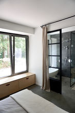 Salle de bain dans la chambre. Division vitrée pour salle de bain. Ensemble de douche chrome. Douche à l'italienne dans la chambre. Plancher béton. Céramique gris foncée.