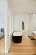 Baignoire autoportante noire et blanche. Douche vitrée. Mur en brique dans salle de bain. Salle de bain mitoyenne à la chambre. 