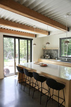 Cuisine avec poutre apparente. plafond en tôle industrielle blanche. Lampe suspendue au dessus de l'îlot de cuisine.
îlot cuisine en corian et bois. Tabouret de bar noir.plancher cuisine en béton