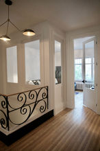 Rambarde noire escalier .
rambarde metal et bois. Lampe suspendue design au dessus escalier.
parquet en bois. Moulures blanches autour des portes