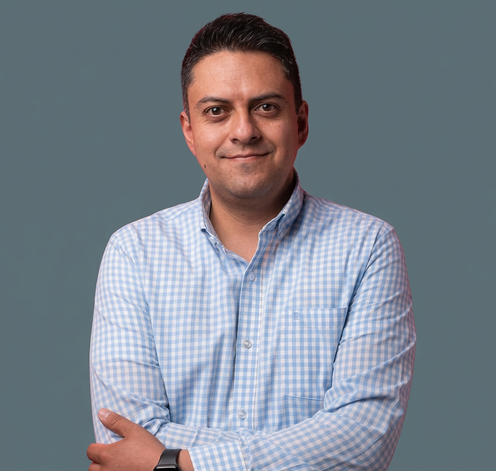 Studio photography of a man smiling confidently. He is wearing a checkered shirt and has his arms crossed, looking directly at the viewer.