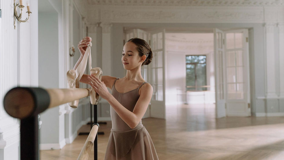 Ballerina adjusting pointe shoes in a bright, spacious ballet studio, showcasing grace and focus.