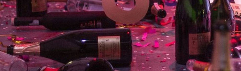 Algumas garrafas de vinho e champagne espalhadas aleatoriamente com confetes, pedaços de papel e enfeites de festa espalhados, aparentando que uma grande festa aconteceu ali.