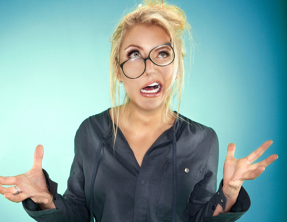 Blonde woman in oversized glasses and dark shirt, making a surprised face with raised hands against a blue gradient background.