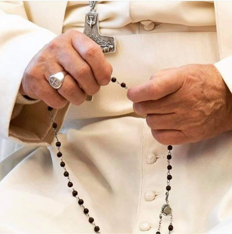Detalhe da foto do Papa Francisco, recortando suas mãos segurando o Santo Terço em posição junto à seu Crucifixo Papal sobre sua batina branca papal.
