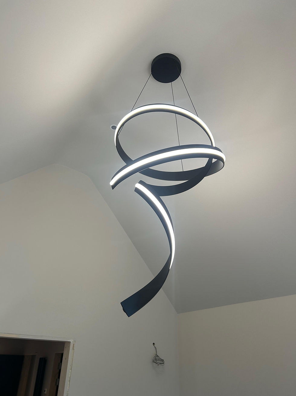 Black ribbon-style spiral LED pendant light installed above a vaulted stairwell, Camberley, Surrey