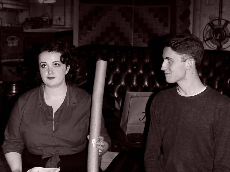 Comedic Image of Rachel Eben holding a pool noodle upright and George Bootle amused.