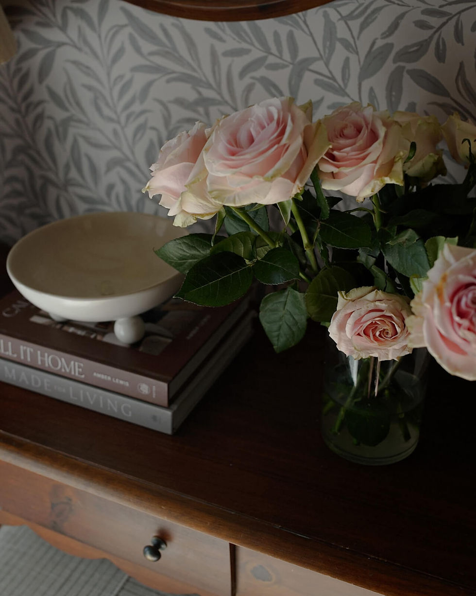 Florals beside a bowl with books stacked, placed delicately in front of Artza vintage floral print wallpaper