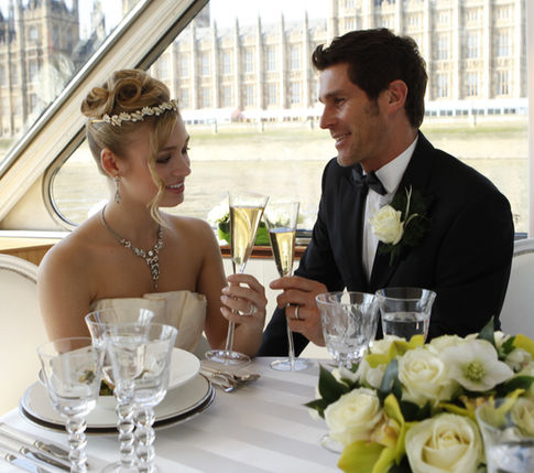 Bride with a tiara and soft updo toasting with her groom on a river boat in London
